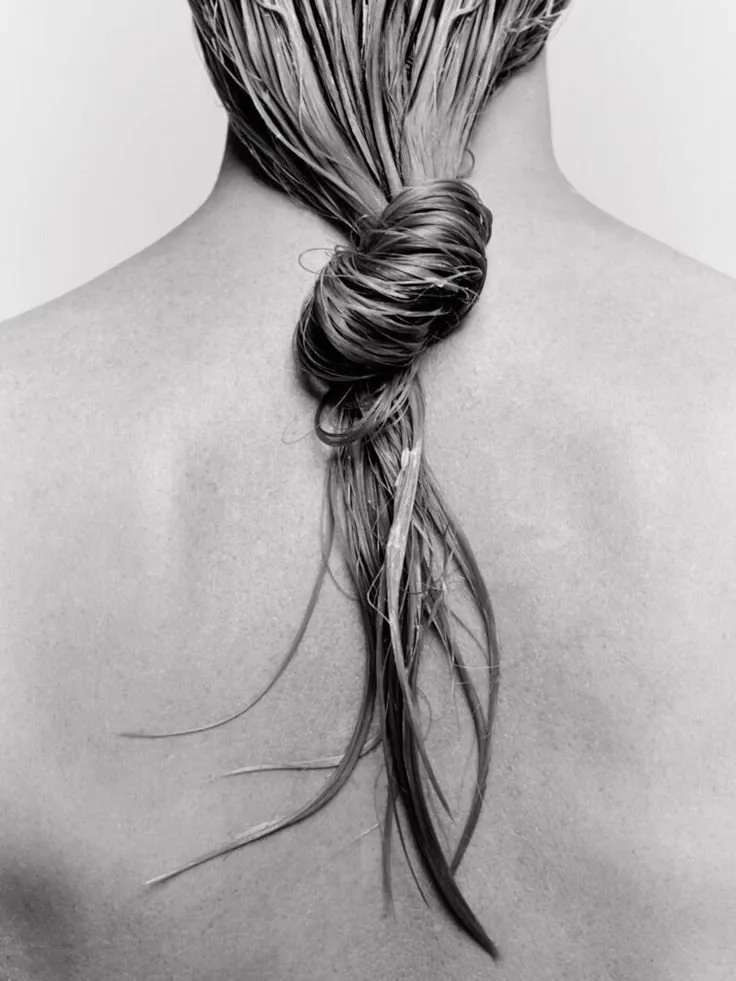 A neatly coiled hairstyle is styled low at the nape of a bare neck