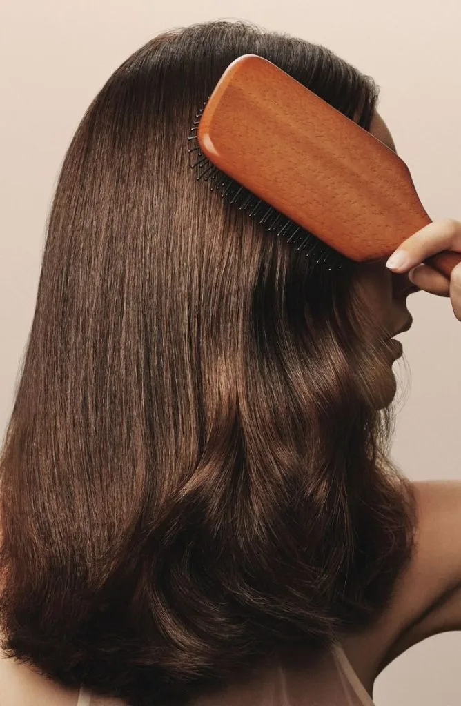 Long, smooth brown hair is being brushed with a wooden paddle brush