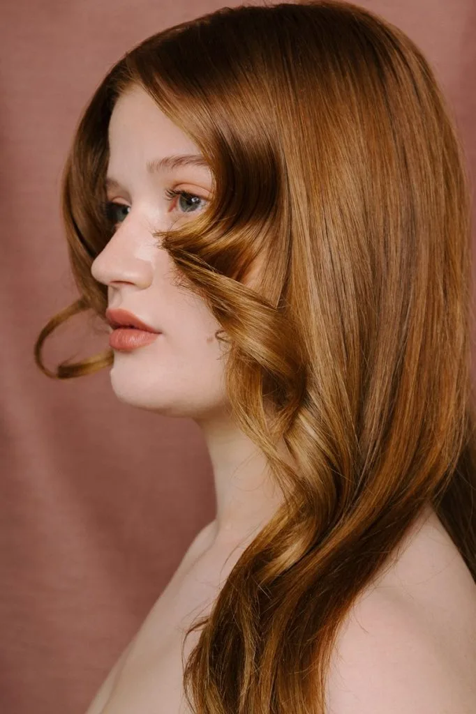 A woman with long, wavy red hair gazes thoughtfully to the side