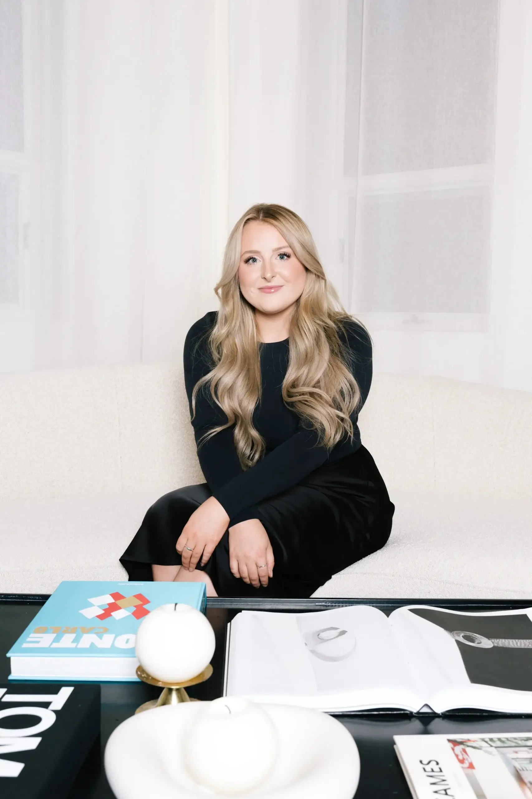 A woman with long hair sits thoughtfully on a stylish sofa beside fashionable decor