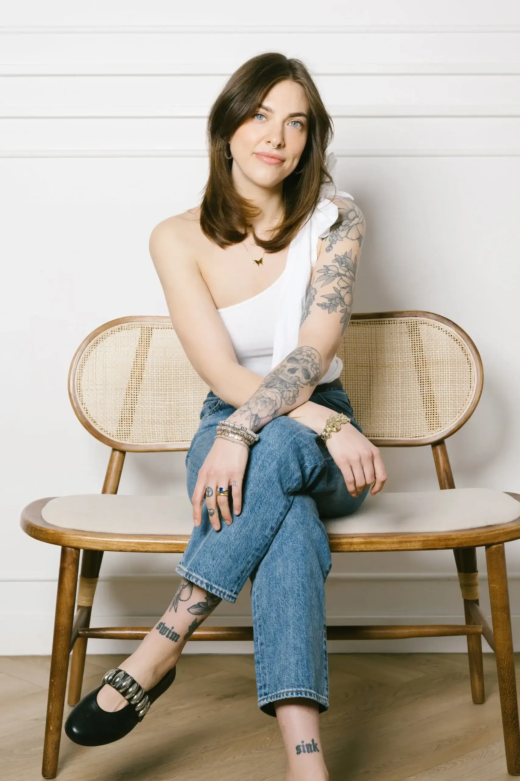 A woman sits confidently on a wooden bench, showcasing her tattoos and stylish outfit