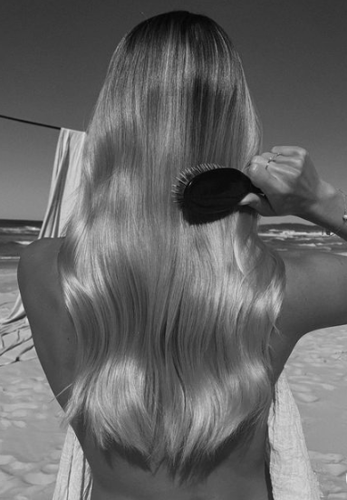 Long, flowing hair is gently brushed while standing by the beach