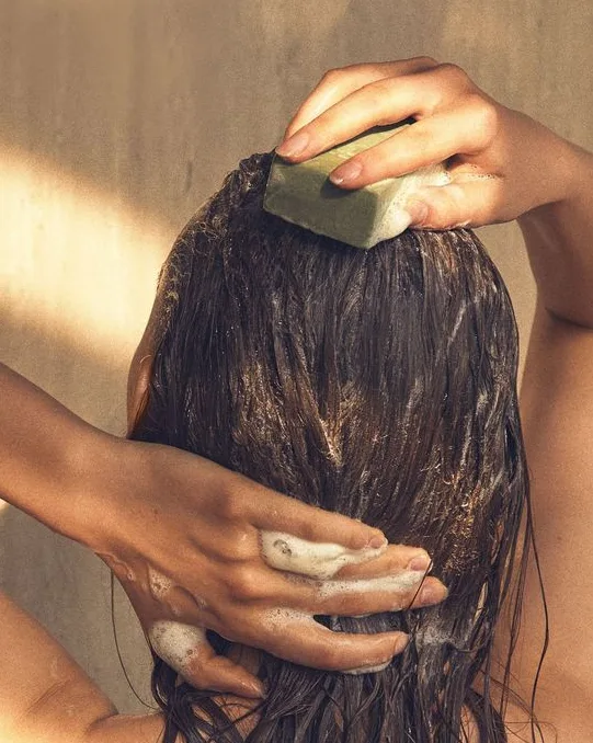 A person washes their hair with a bar of shampoo while massaging their scalp