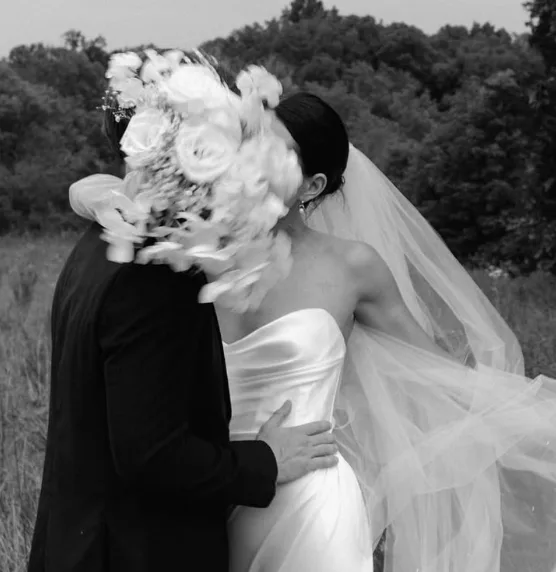 A couple shares an intimate moment, partially obscured by floral arrangements and flowing fabric