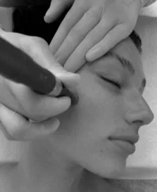 A person receiving a facial treatment with hands delicately applying a tool to their face