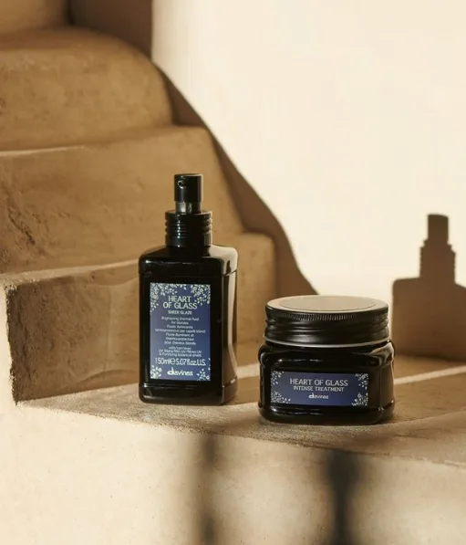 Two dark cosmetic containers sit on a textured stone ledge, casting shadows