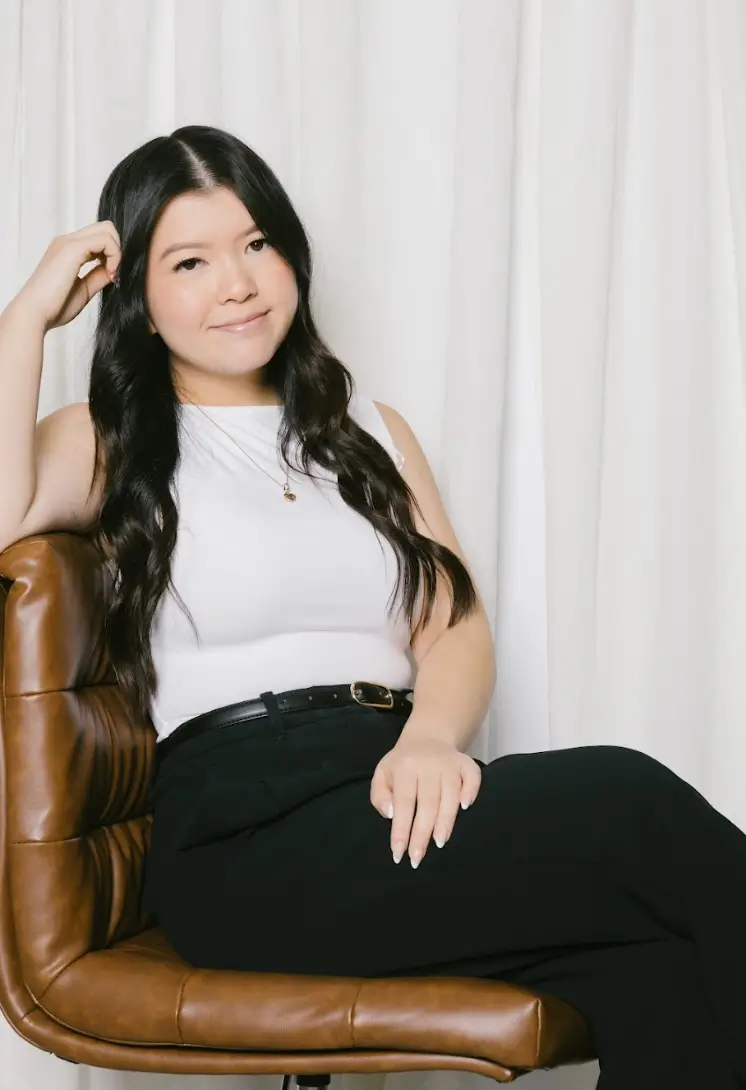 A young woman with long hair sits confidently in a stylish chair