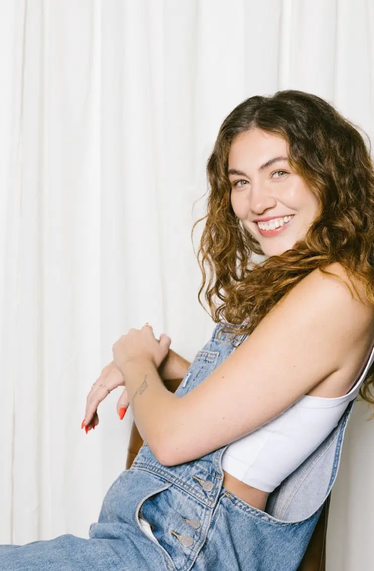 A woman with curly hair smiles while sitting on a chair