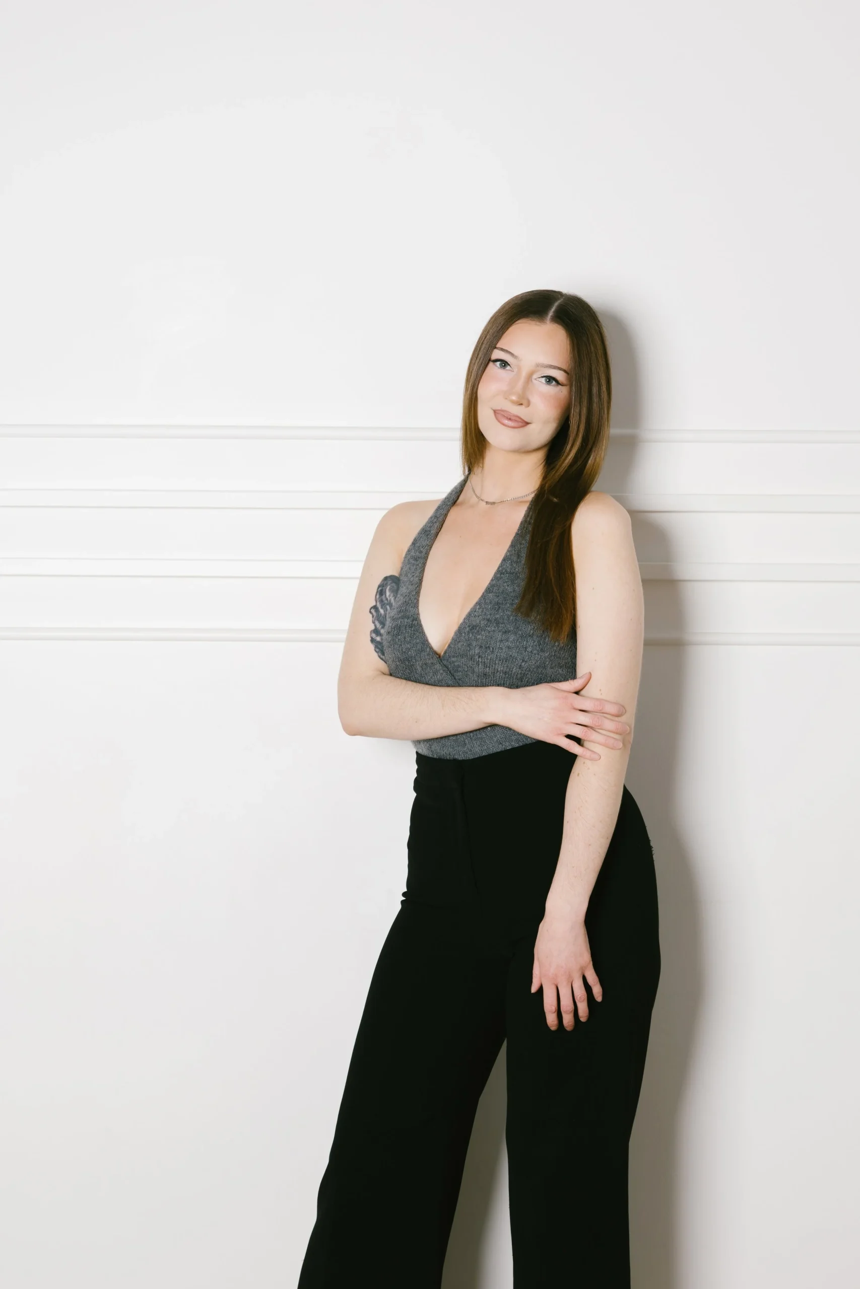 A person stands confidently against a simple, light-colored background, wearing stylish attire