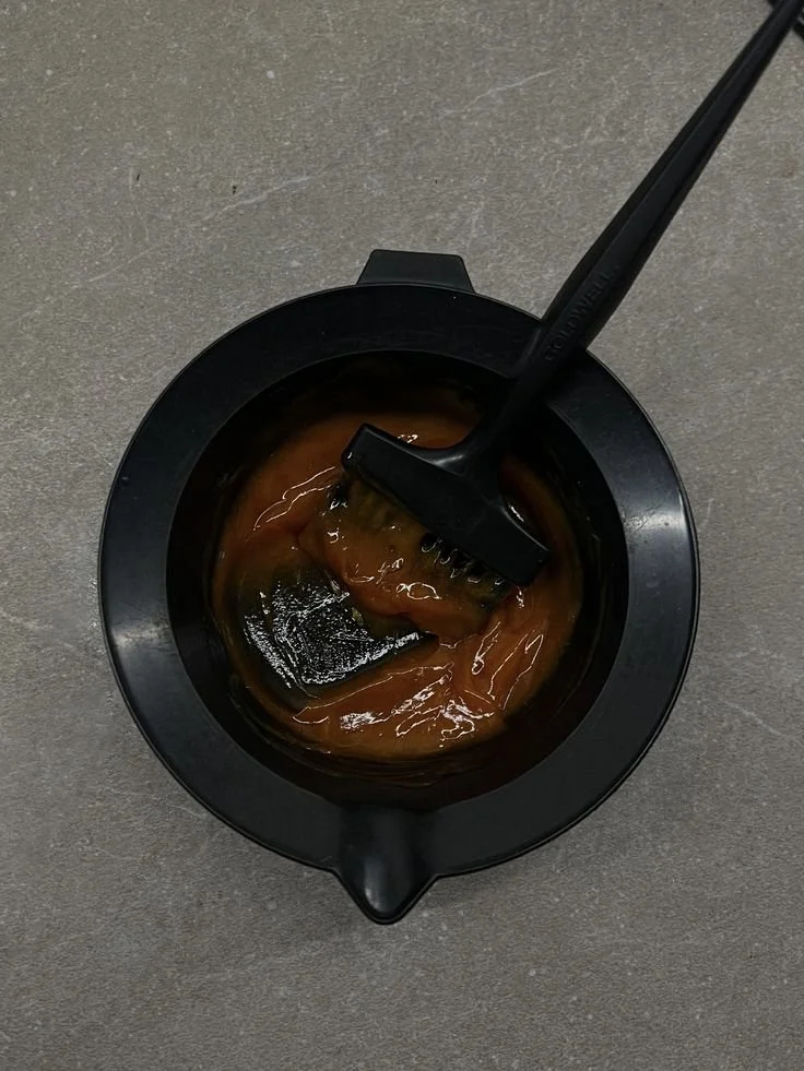 A black bowl contains a thick reddish-brown mixture with a brush resting inside