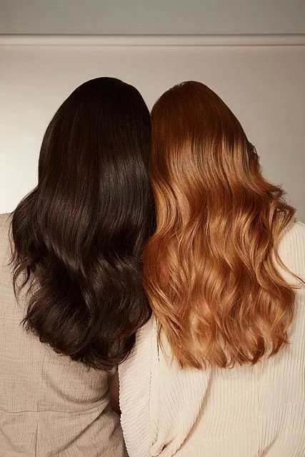 Two women stand closely together, showcasing their distinct hairstyles and hair colors from behind