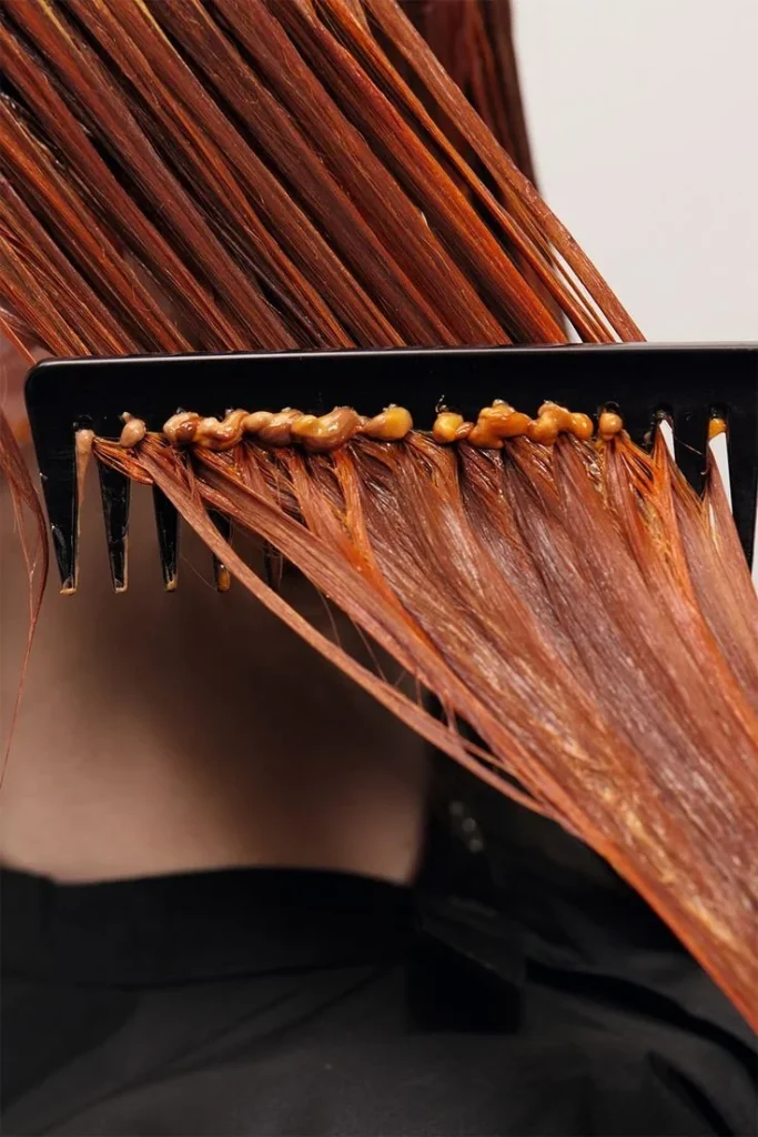 Bright orange hair dye is being applied to strands with a comb