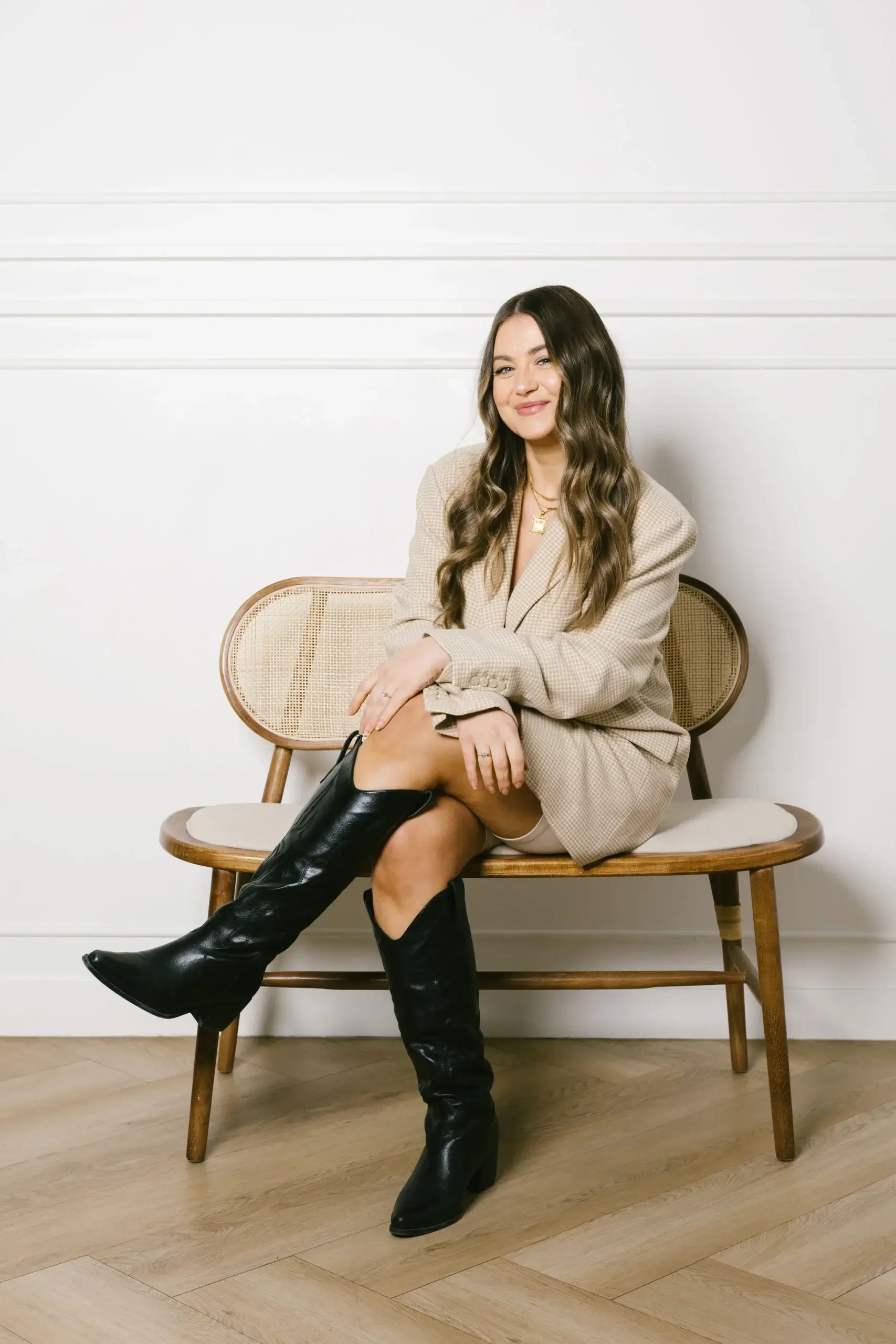 A woman with wavy hair poses confidently while sitting on a stylish chair