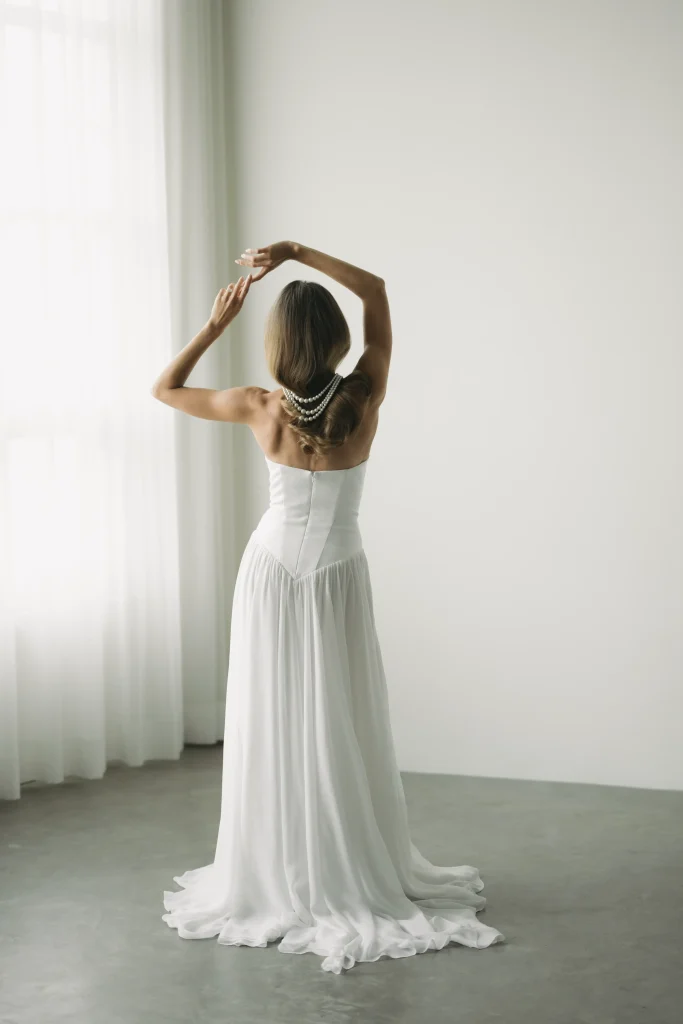 A woman in a flowing white dress poses gracefully with her arms raised