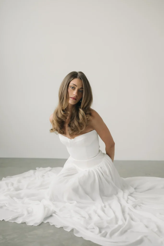 A woman in a white dress sits gracefully on the floor, gazing thoughtfully