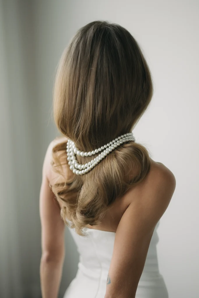 A woman with elegant, flowing hair wears layered pearl necklaces