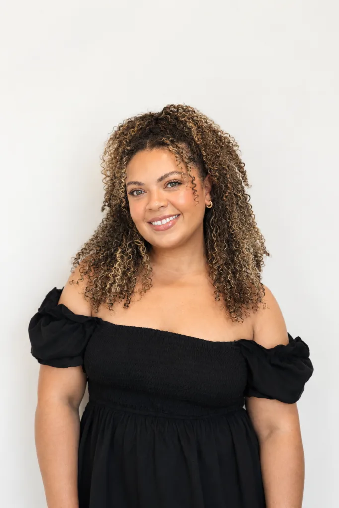 A woman with curly hair smiles while wearing an off-the-shoulder black dress