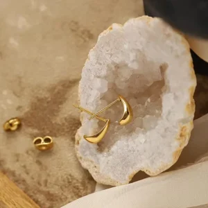 Gold earrings rest on a geode slice, surrounded by neutral textures