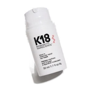 A sleek white bottle contains a hair treatment with bold black and red lettering