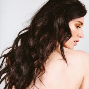 A woman with long, wavy hair poses gracefully, showcasing her profile