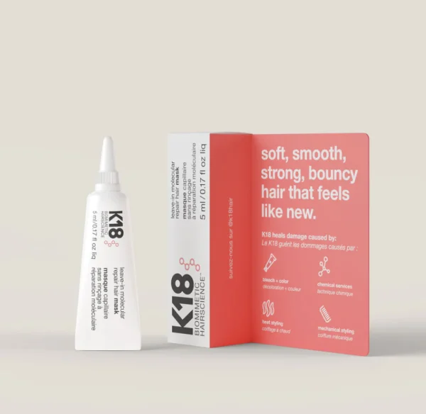 A tube of hair treatment stands beside its red-and-white packaging on a neutral background