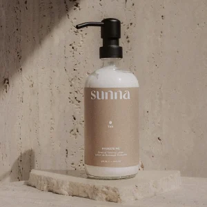 A stylish lotion bottle rests on a textured stone surface against a minimalist backdrop