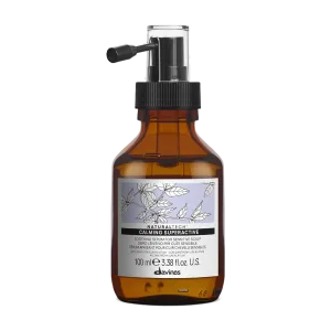 A brown glass bottle with a pump contains a calming hair product, decorated with botanical illustrations